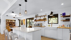 A modern kitchen with white cabinetry, a central island, pendant lighting, and built-in shelves. - Red Bird Cottage- Convenient 2/1 with Outdoor Space (Wimberley)