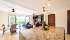Una cocina moderna con encimera de granito, un comedor con mesa de vidrio y una sala de estar con sofá y televisor.