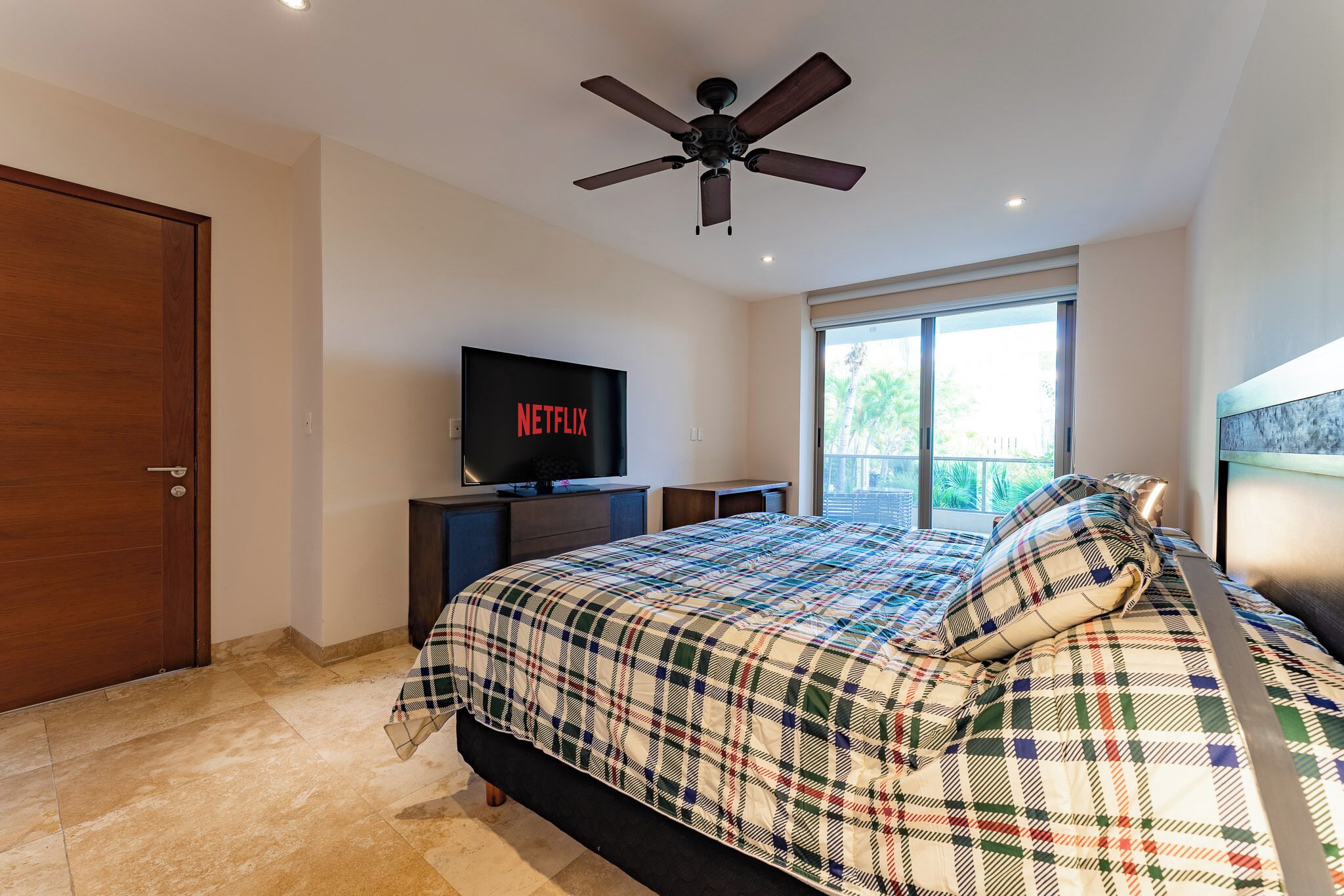 Un dormitorio con cama, televisión, ventilador de techo y ventana.