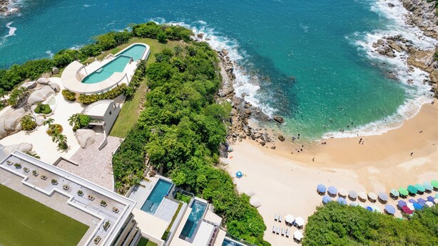 Vista aérea de un complejo turístico costero con piscina, playa y vistas al océano.