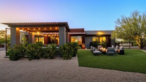 Una casa moderna con un porche cubierto, mobiliario de exterior y un césped bien cuidado.