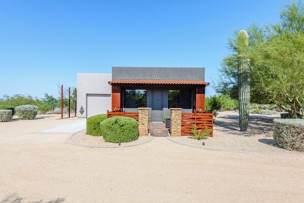 A modern house with a covered porch, a garage, and a well-maintained garden with cacti and shrubs.