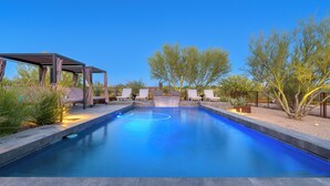 Una piscina con una pérgola y sillas de descanso, rodeada de vegetación desértica.