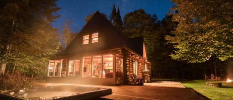 A log cabin with a hot tub and a fire pit in the yard.