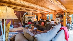 A log cabin interior with a stone fireplace, wooden ceiling beams, and a cozy seating area. - The Beaver Lodge by Escapades Tremblant (Lac-Superieur)