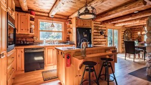 A rustic cabin interior with wooden walls and ceilings, a kitchen with wooden cabinets and a built-in dishwasher, a bar area with stools, and a dining area with a table and chairs. - The Beaver Lodge by Escapades Tremblant (Lac-Superieur)