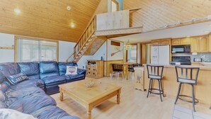 A spacious living area with a wooden ceiling, a sofa, a coffee table, and a kitchen area with a microwave and refrigerator. - ARROWHEAD LAKE - Ski Chalet- Gameroom, Firepit - Lake View, Walk to Beach/Island (Pocono Lake)