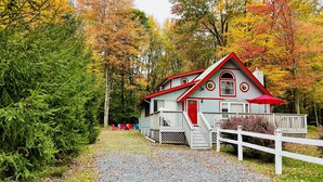 A cabin with a red roof and white walls, surrounded by trees with autumn foliage. - ARROWHEAD LAKE - Ski Chalet- Gameroom, Firepit - Lake View, Walk to Beach/Island (Pocono Lake)