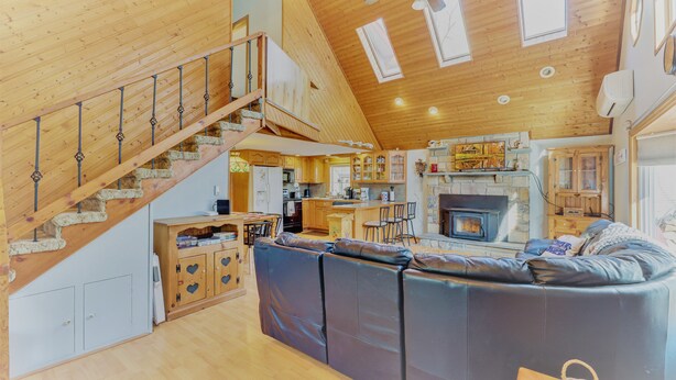 A spacious living area with a large sofa, wooden staircase, kitchen, and a fireplace. - ARROWHEAD LAKE - Ski Chalet- Gameroom, Firepit - Lake View, Walk to Beach/Island (Pocono Lake)