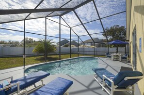 Een zwembadgedeelte met blauwe ligbedden, een overdekte zithoek met tafels en stoelen, en uitzicht op de omgeving.