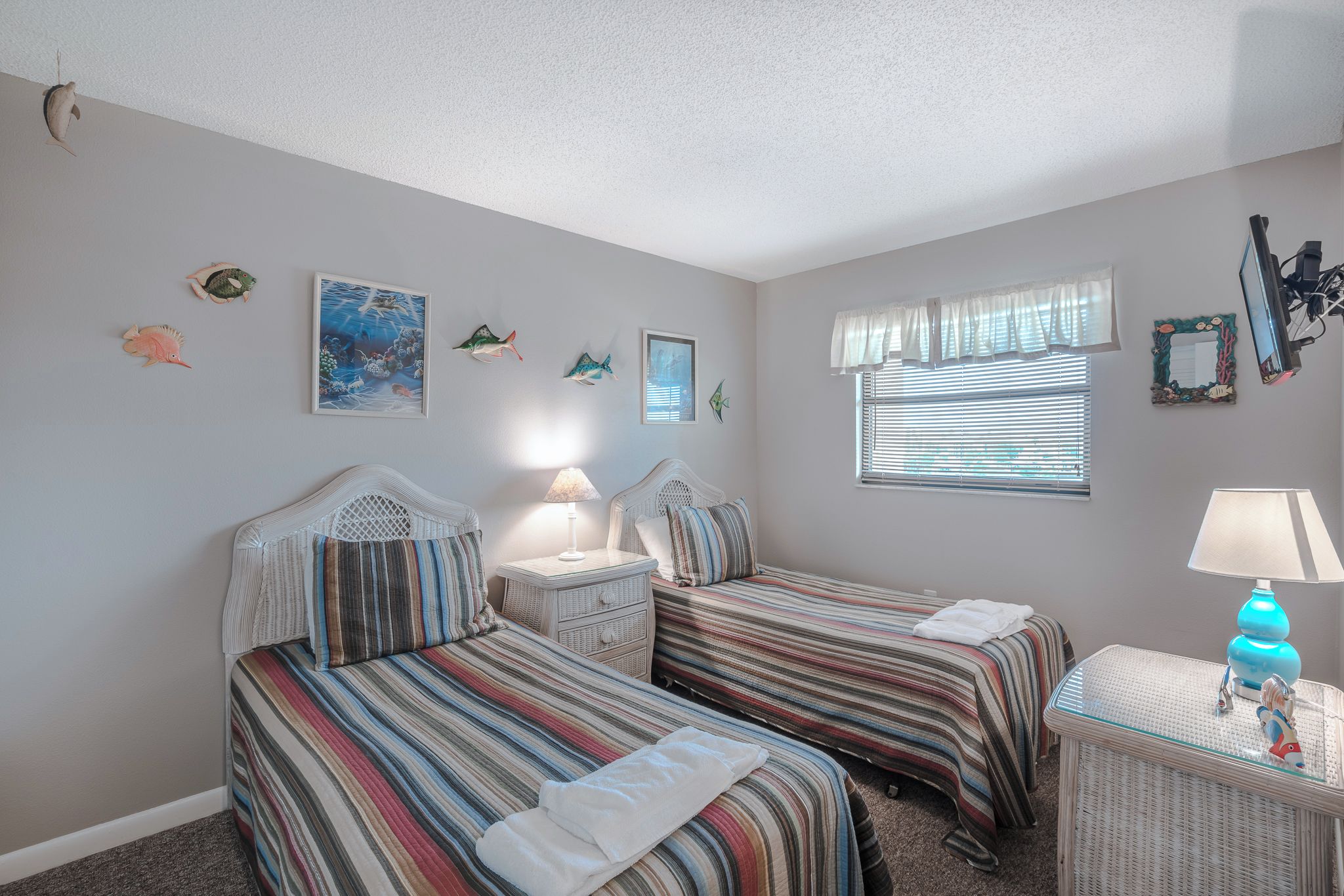 A bedroom with two beds, a nightstand, a lamp, and wall decorations including fish and a framed picture.