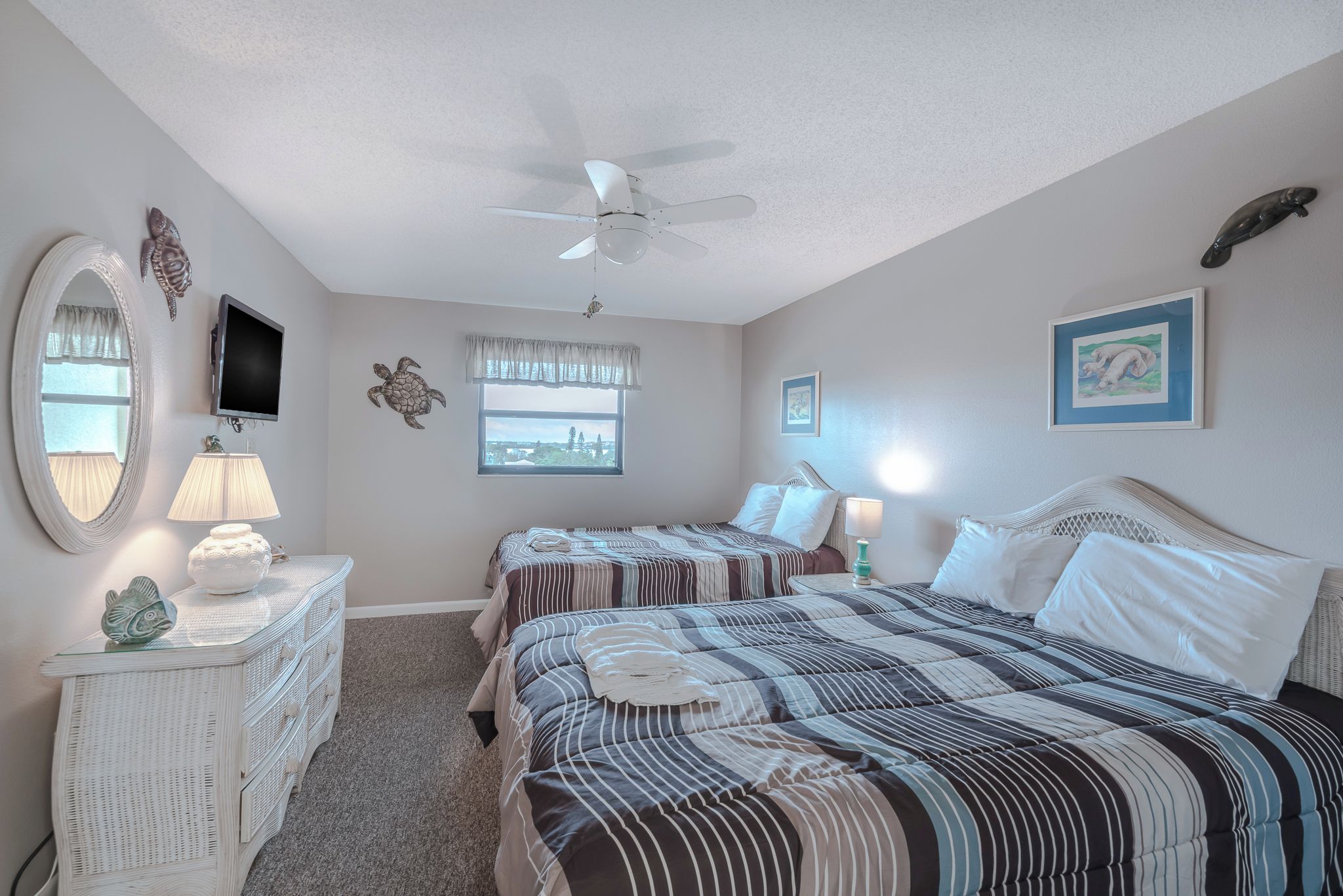A bedroom with two beds, a ceiling fan, a dresser, a TV, and a window with a view.
