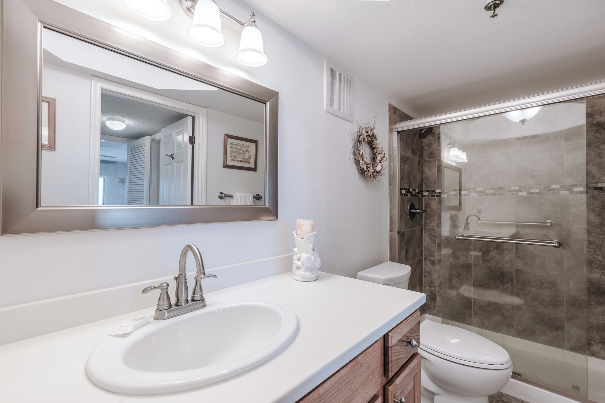 Une salle de bain avec un lavabo blanc, un grand miroir, des toilettes et une douche à parois de verre.