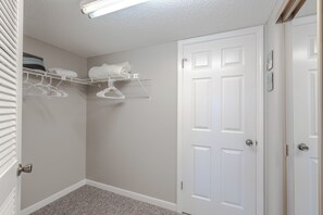 A walk-in closet with a white door, a hanging rack with folded towels, and a light fixture on the ceiling.
