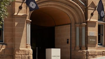 Enter through the grand archway of The Tasman, flanked by flags and a classic stone facade.