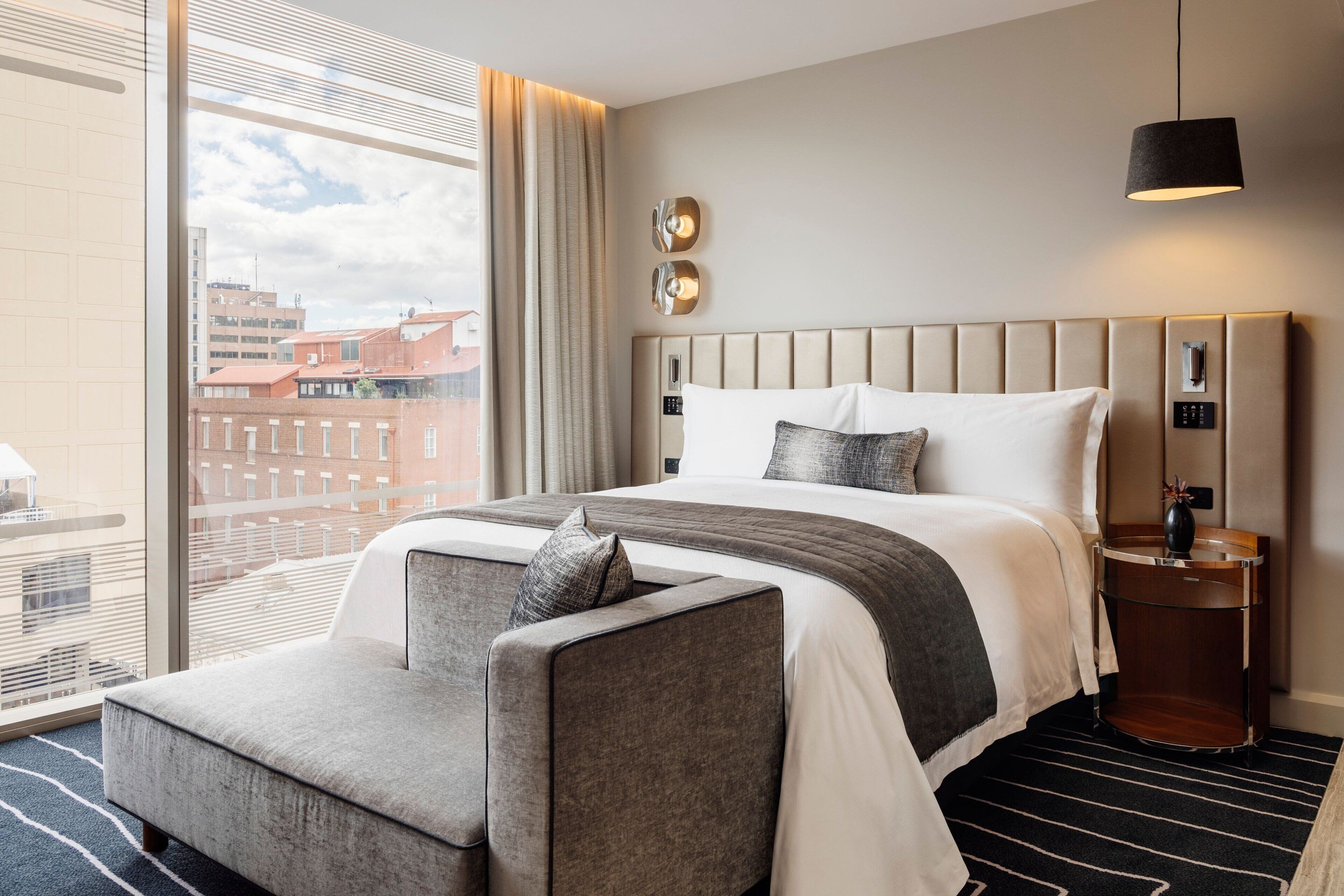 Une chambre d’hôtel moderne dotée d’un grand lit, d’un coin salon, d’une table de chevet et offrant une vue sur le paysage urbain.