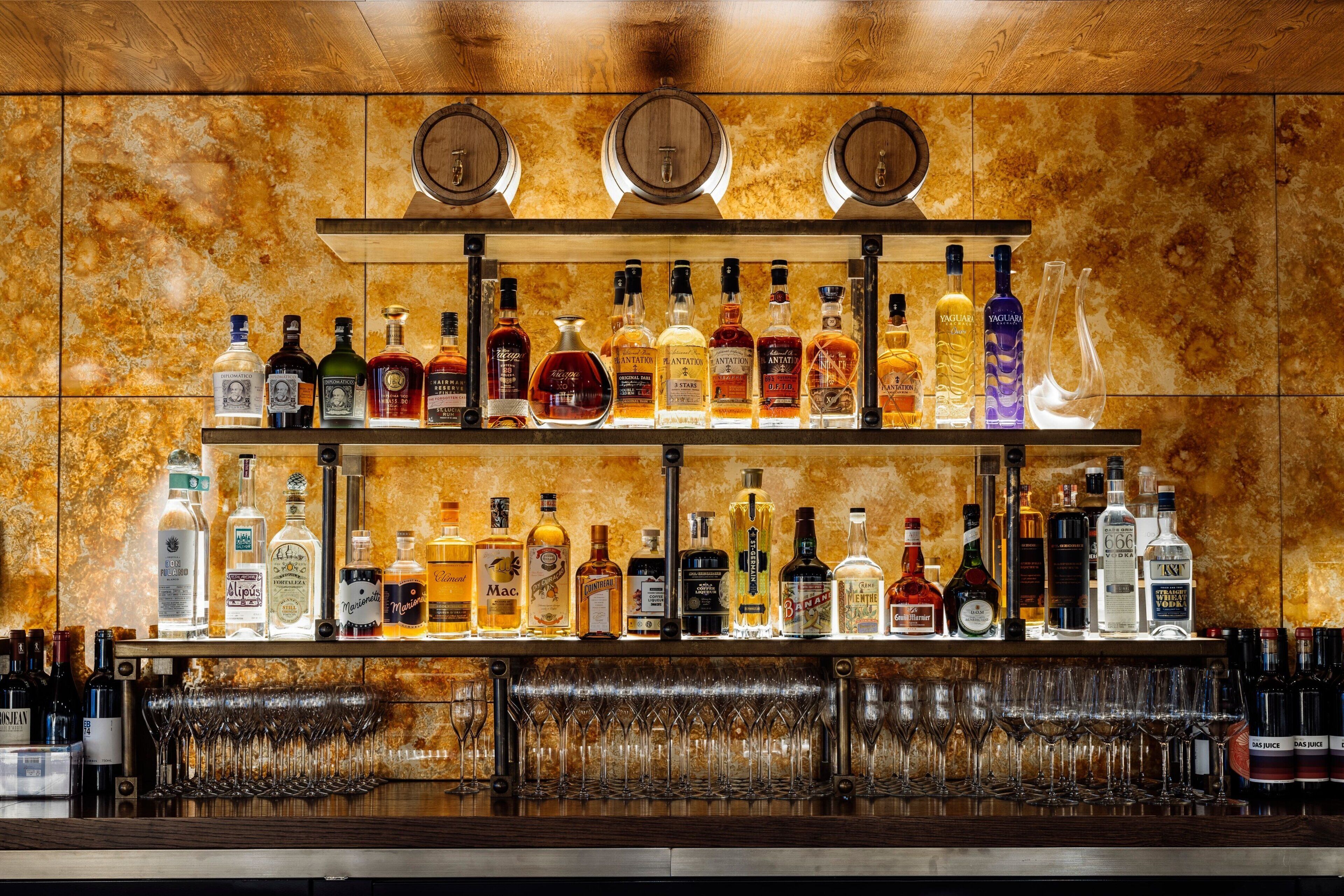 Eine Bar mit mehreren Regalen voller Spirituosenflaschen und einer Reihe von Gläsern.