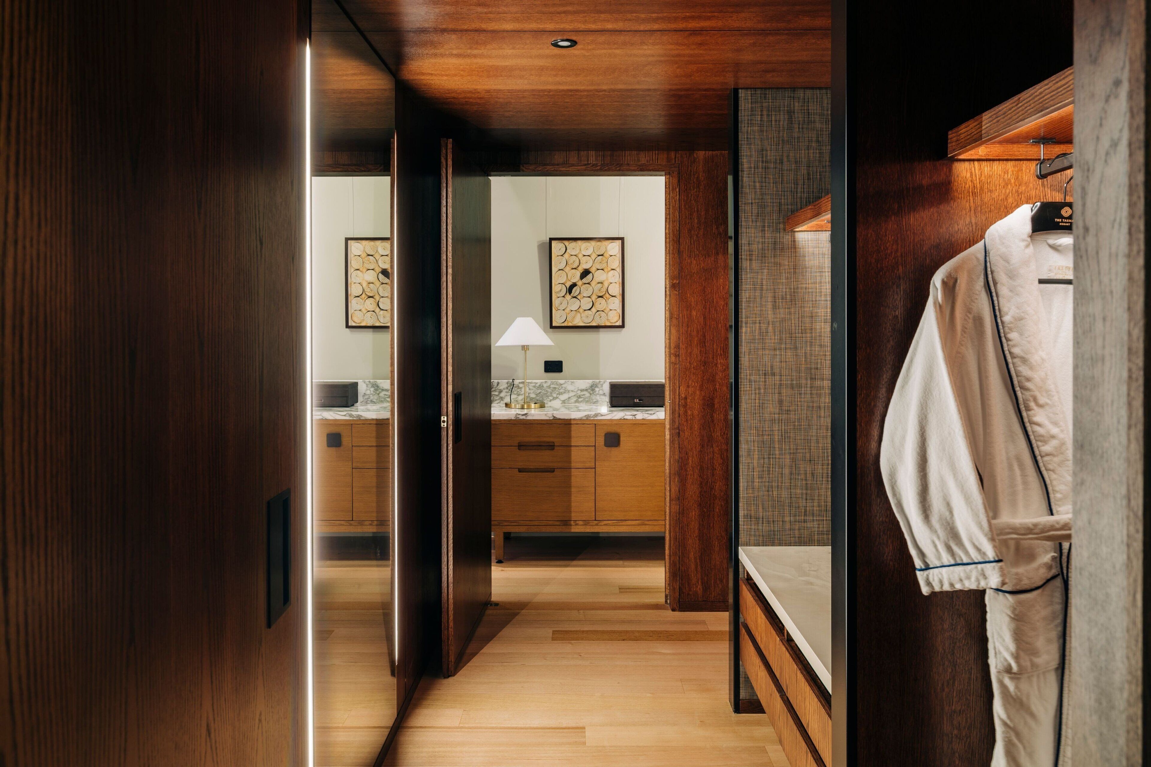 A modern bathroom with wooden cabinetry, a marble countertop, and a hanging robe.