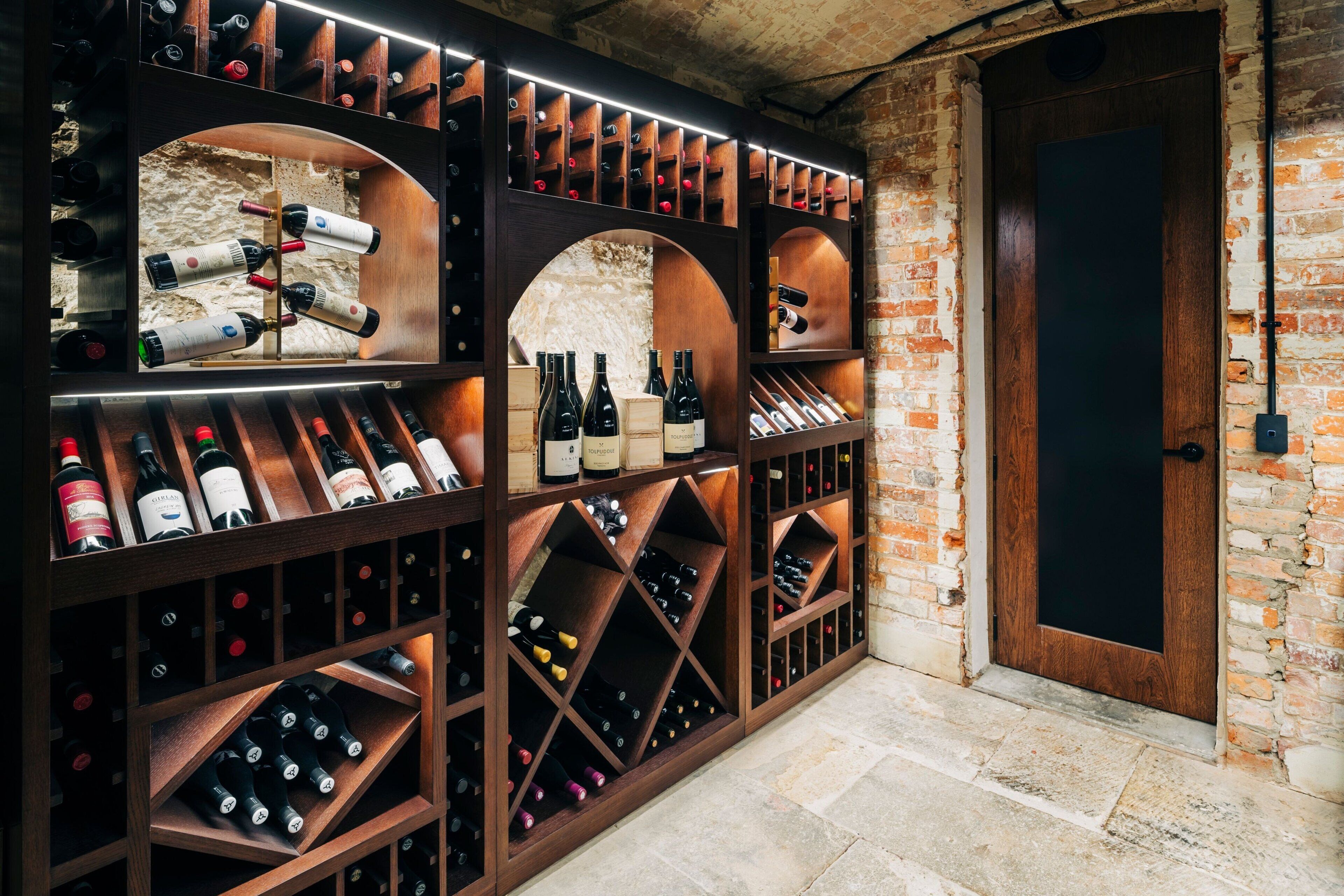 A wine cellar with wooden racks and bottles, a brick wall, and a wooden door.