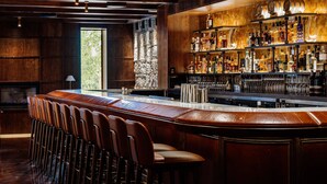 Een bar met een lange toonbank, verschillende krukken en een goed gevulde flessenkast.