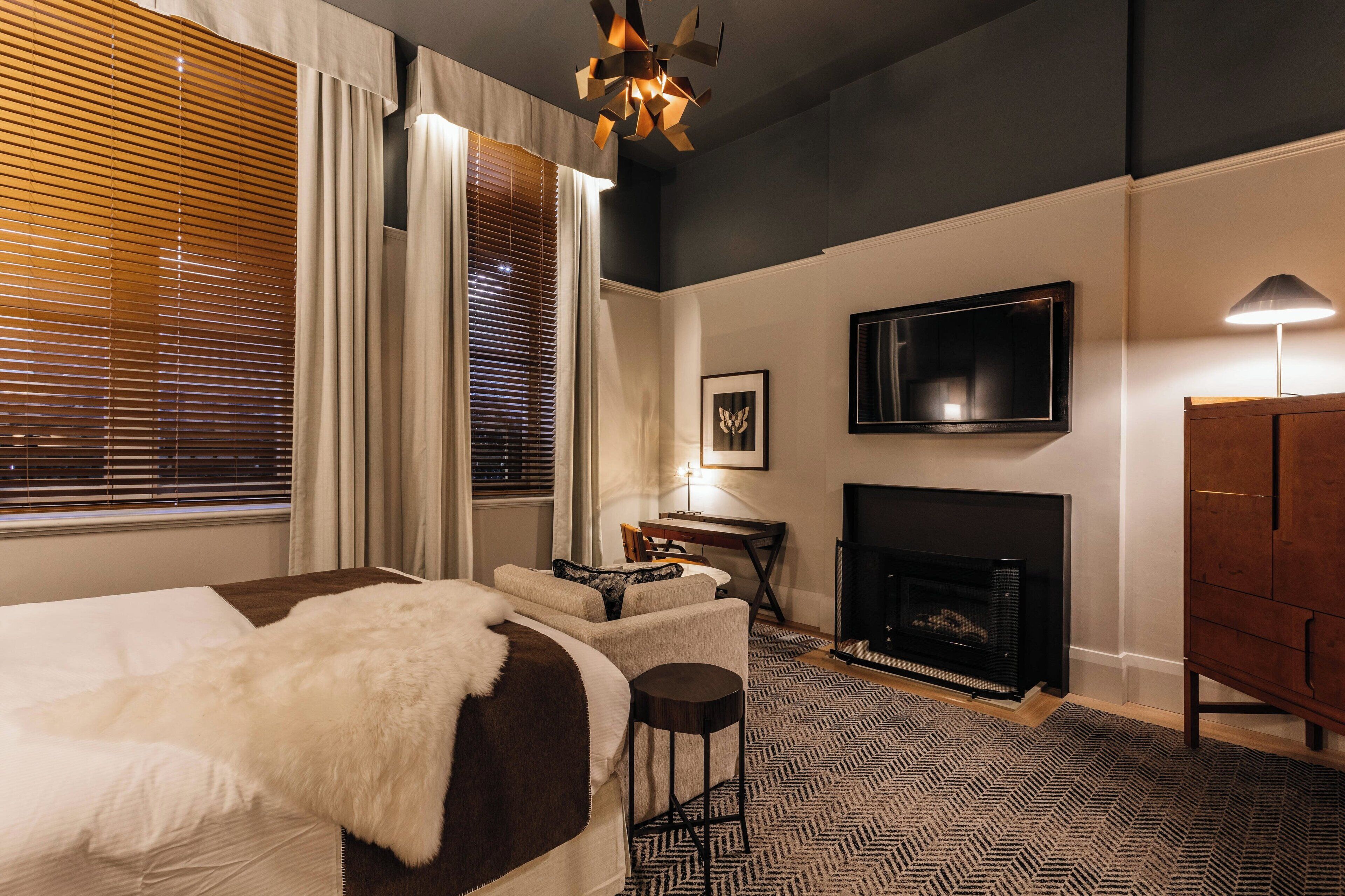 A bedroom with a bed, a desk, a TV, and a fireplace.