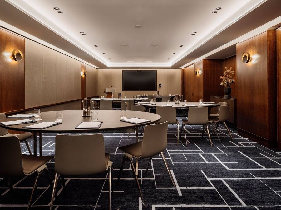 A conference room with round tables, chairs, and a large flat-screen TV.