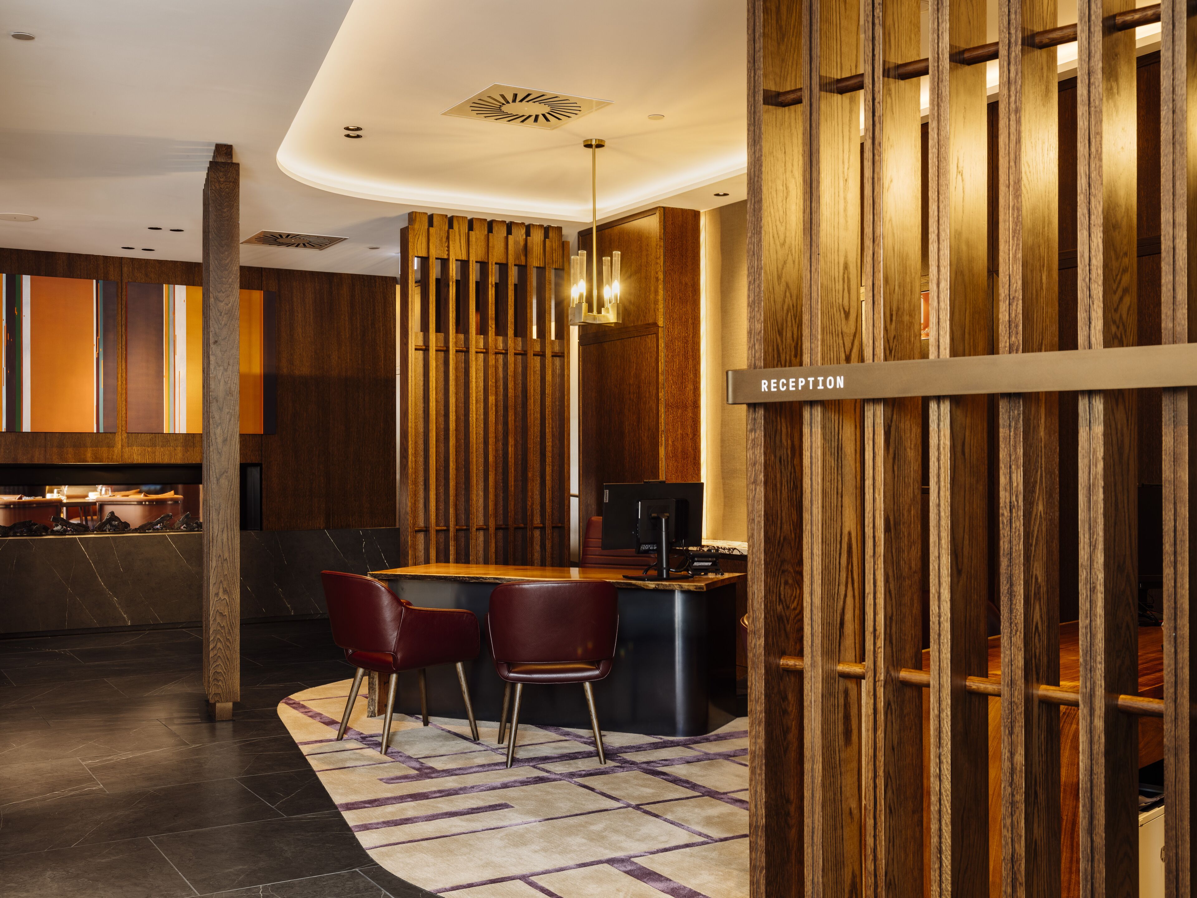 Una moderna zona de recepción con un mostrador de madera, dos sillones de cuero y un cartel que indica la recepción.