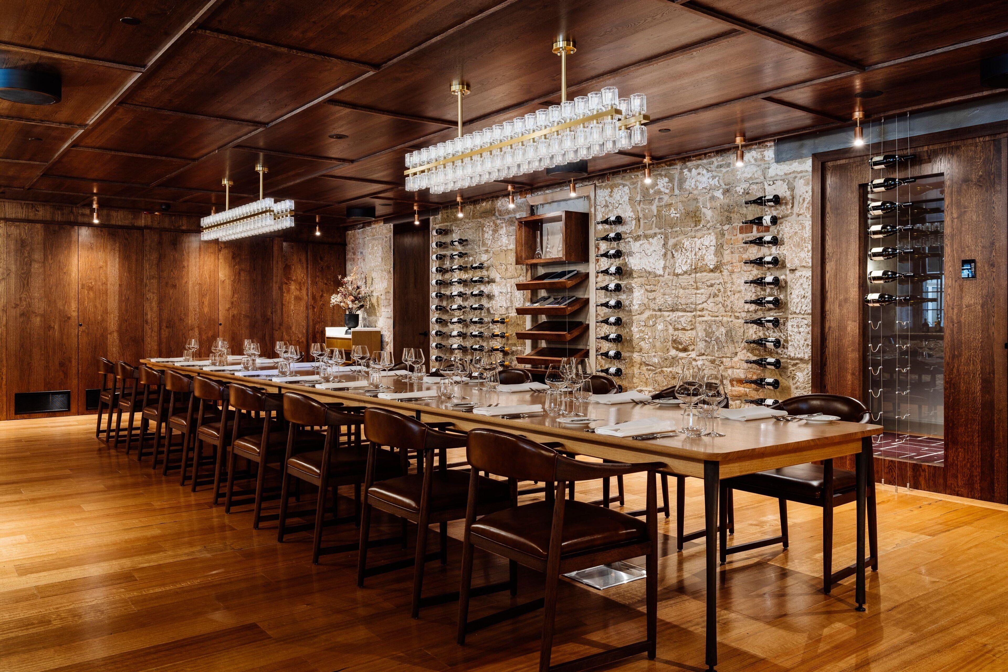 A long dining table set with chairs, wine racks on the walls, and a stone wall.