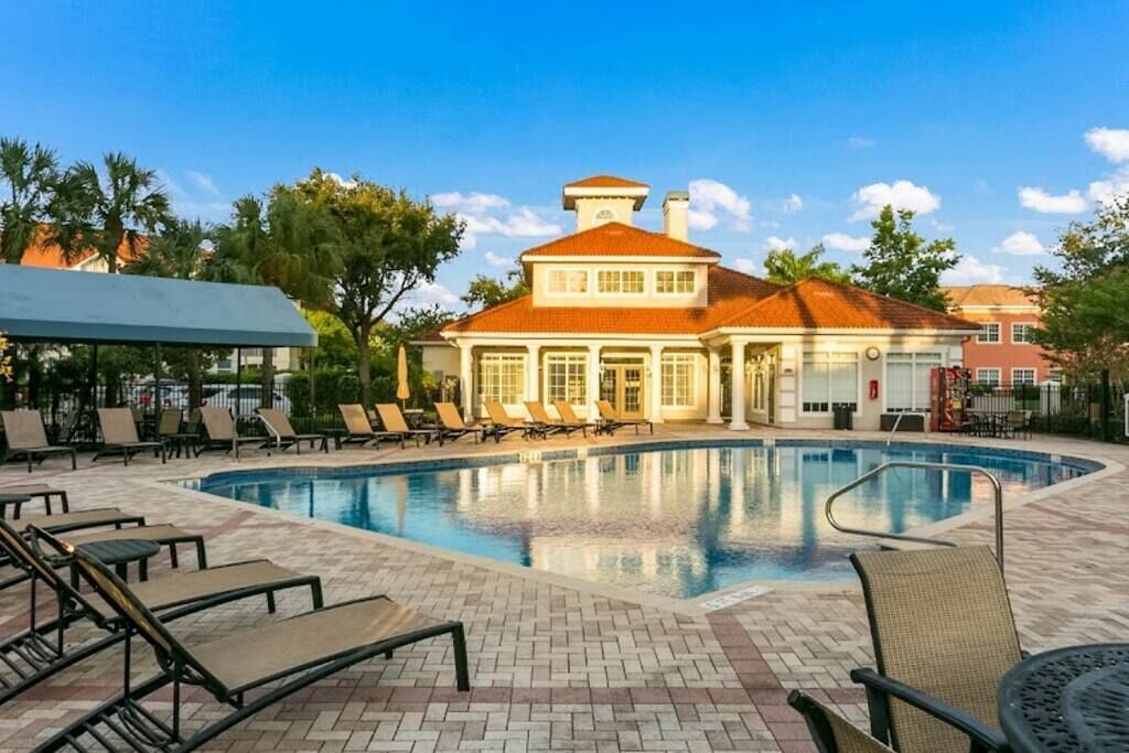 Ein Schwimmbecken mit Liegestühlen und ein Gebäude mit rotem Dach im Hintergrund.