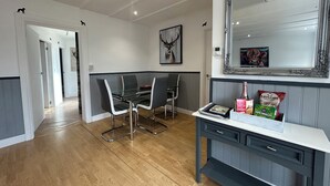 A modern kitchen with a dining area, wooden flooring, and a large mirror above the counter. - Solway Cottage (Annan)