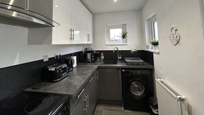 A compact kitchen with a stove, toaster, sink, and a washing machine. - Solway Cottage (Annan)