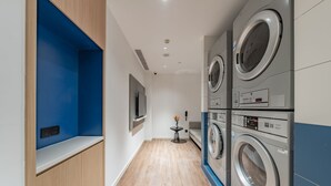 A laundry room with stacked washing machines, a small table with a vase, and a mounted TV. - Holiday Inn Express Shanghai Expo Centre by IHG (Shanghai)