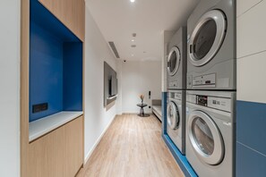 Un cuarto de lavandería con lavadoras apiladas, una mesita con un florero y un televisor montado.