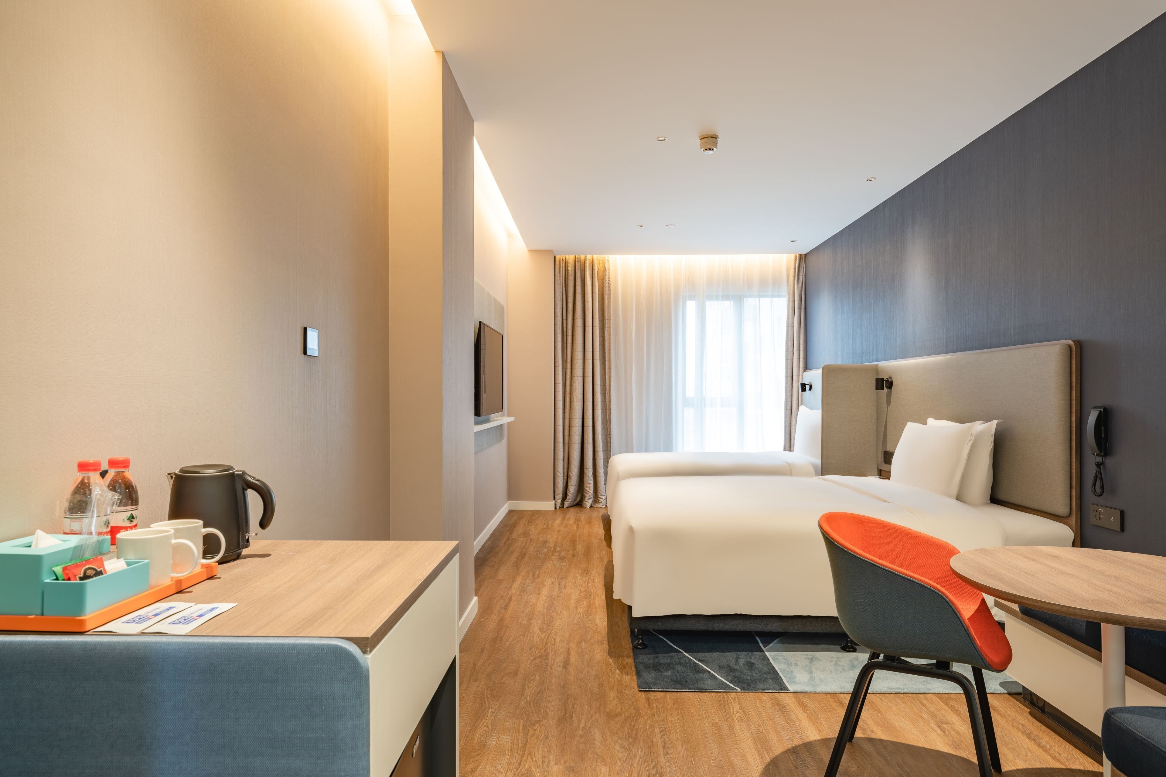 A hotel room with a bed, a desk with a chair, a coffee maker, and a TV on the wall.