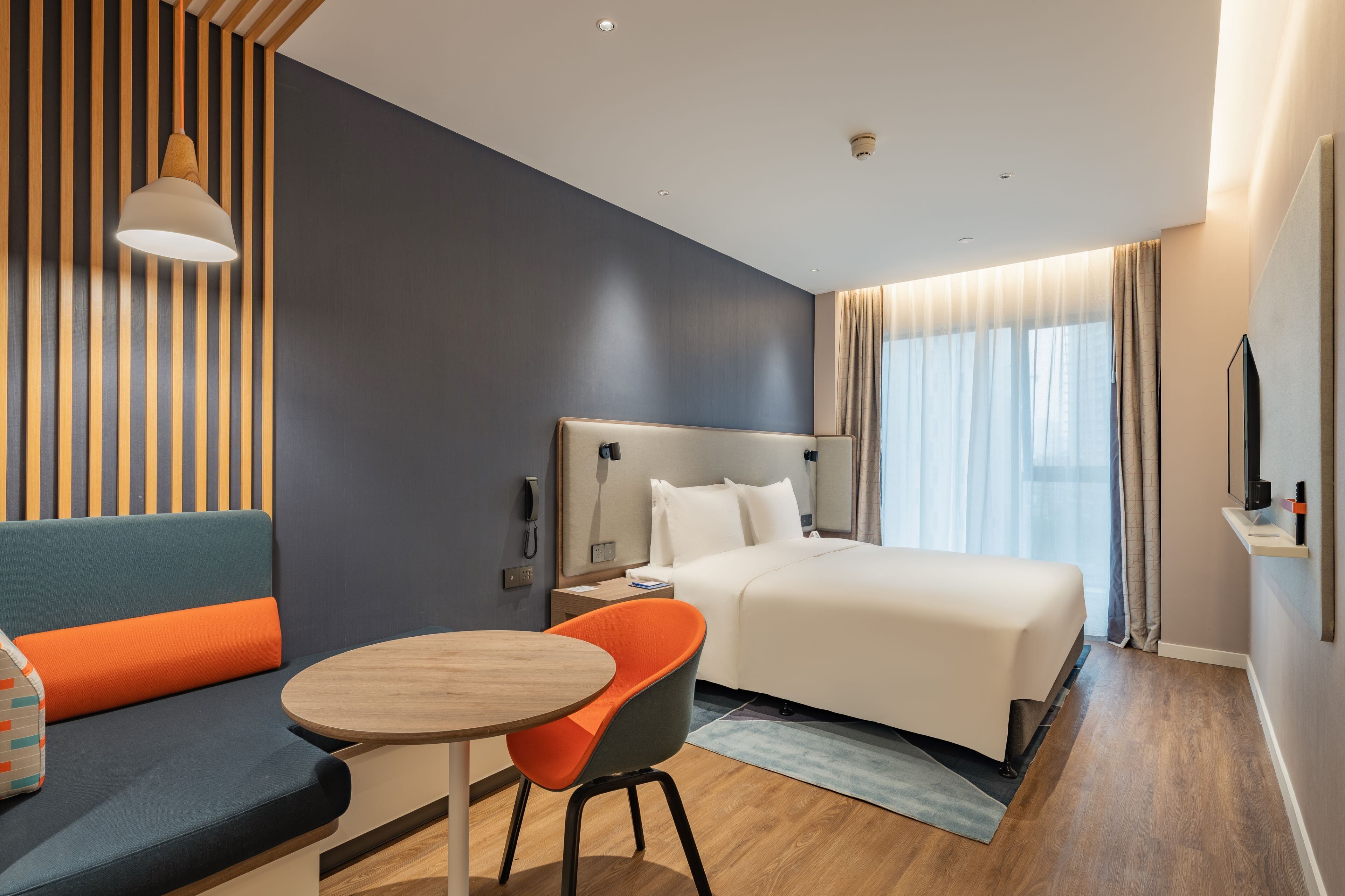 A modern hotel room with a bed, a seating area with a table, and a television on the wall.