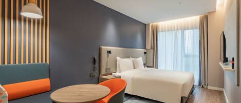 A modern hotel room with a bed, a seating area with a table, and a television on the wall.