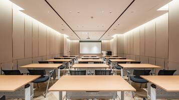 Un salón de conferencias con varias mesas y sillas, una pantalla de proyector e iluminación empotrada en el techo.