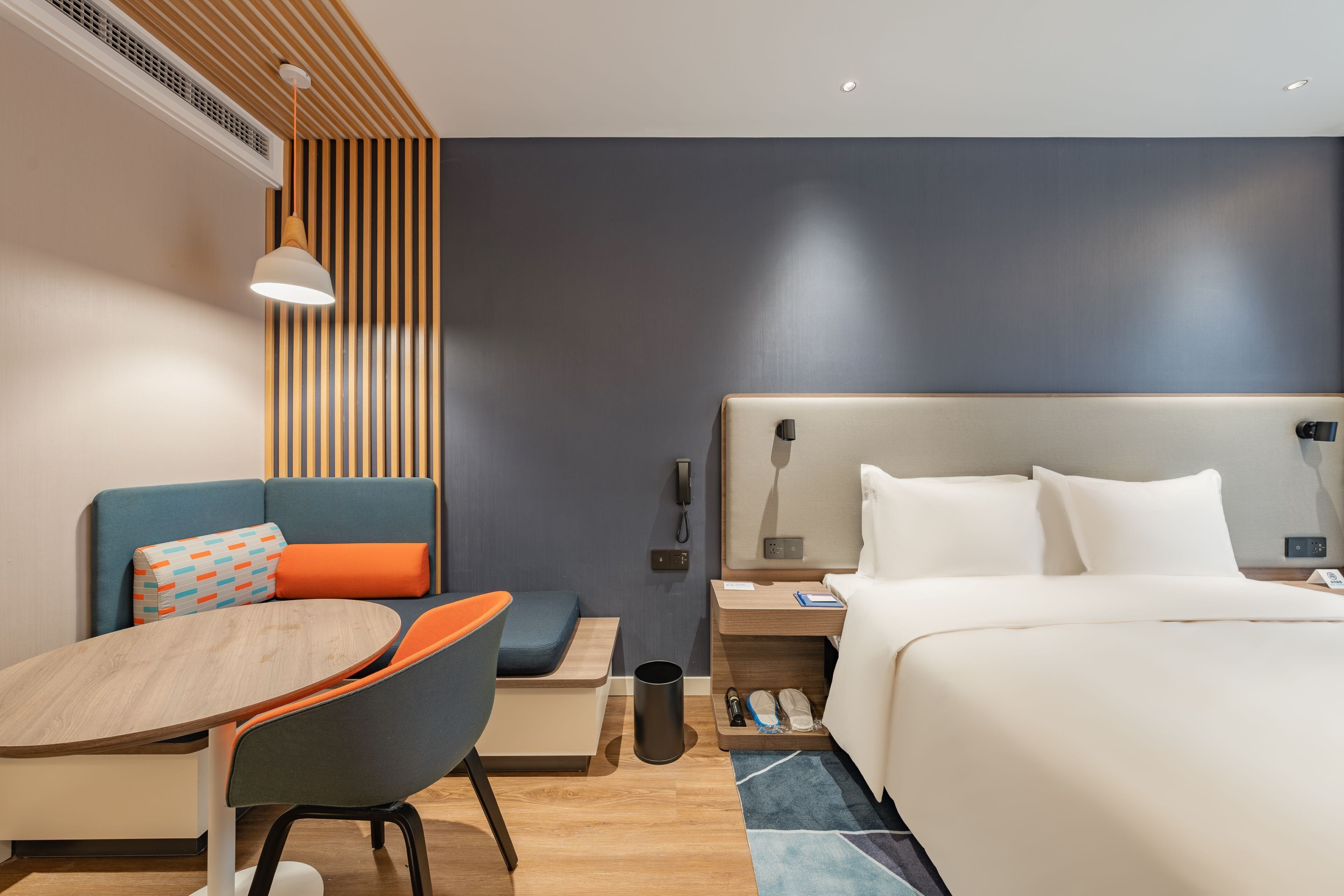 A modern hotel room with a bed, a desk with a chair, a small table, and a sofa.