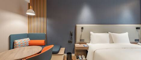 A modern hotel room with a bed, a desk with a chair, a small table, and a sofa.