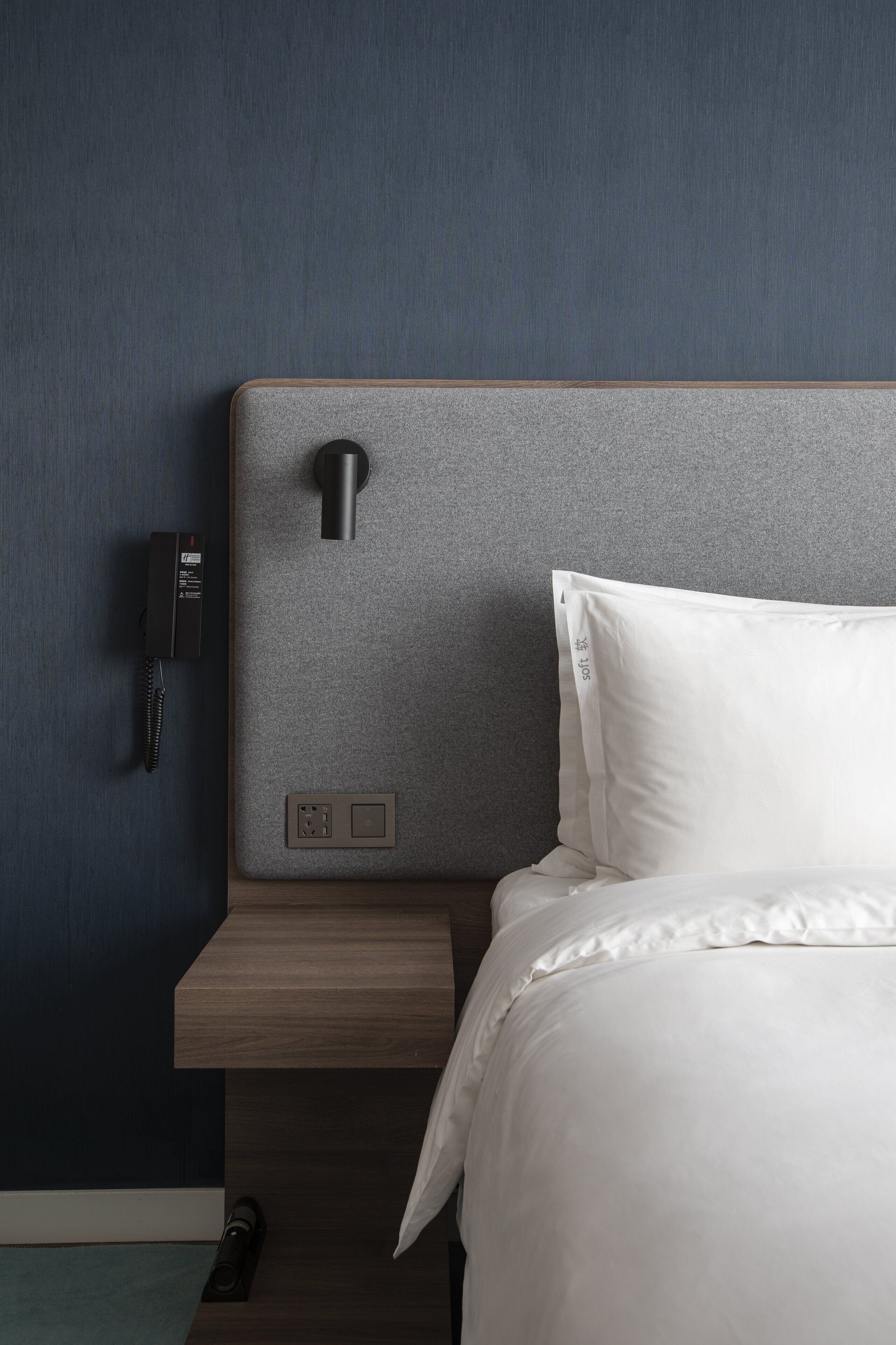 A hotel room with a bed, a bedside table, a phone, and a wall-mounted light.