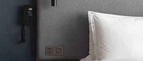 A hotel room with a bed, a bedside table, a phone, and a wall-mounted light.