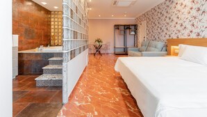 Una habitación de hotel moderna con suelo de mármol, una cama grande, baño con mampara de vidrio y armario con espejo.
