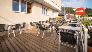 Un patio al aire libre con mesas y sillas, un edificio con el rótulo 'Café' y una señal de 'No Entrar' al fondo.
