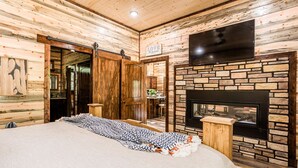 Ein schlafzimmer im Blockhausstil mit einem großen Bett, einem Kamin und einem an der Wand befestigten Fernseher.