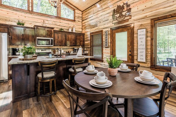 A wooden cabin interior with a kitchen, dining area, and a sign that reads 'LOVE GROWS BEST IN LITTLE HOUSES JUST LIKE THIS.' - Calvert's Copper Cabin, Cozy cabin! Hot tub, Free Firewood, Fireplace! (Broken Bow)