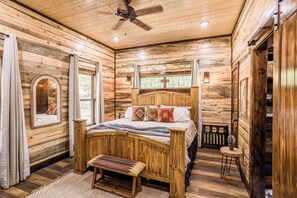 A wooden cabin bedroom with a bed, bench, and ceiling fan. - Calvert's Copper Cabin, Cozy cabin! Hot tub, Free Firewood, Fireplace! (Broken Bow)