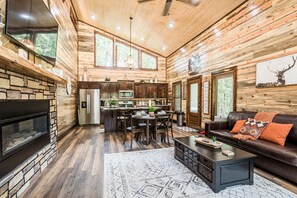 A spacious living area with a fireplace, a dining table, and a cozy seating area. - Calvert's Copper Cabin, Cozy cabin! Hot tub, Free Firewood, Fireplace! (Broken Bow)