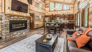 Ein rustikales Blockhaus-Interieur mit Kamin aus Stein, Holzwänden, einem Essbereich und einem gemütlichen Wohnzimmer mit Ledersofa.
