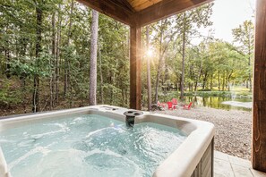 A hot tub in a wooded area with a view of trees and a pond. - Calvert's Copper Cabin, Cozy cabin! Hot tub, Free Firewood, Fireplace! (Broken Bow)