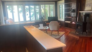 A spacious living area with a wooden floor, a large window, a fireplace, and a built-in bookshelf.